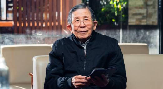 Elderly man smiling while holding a mobile phone.