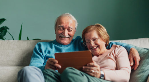 Older man and woman smiling while looking at an electronic tablet. Get Online Week logo in lower right corner.
