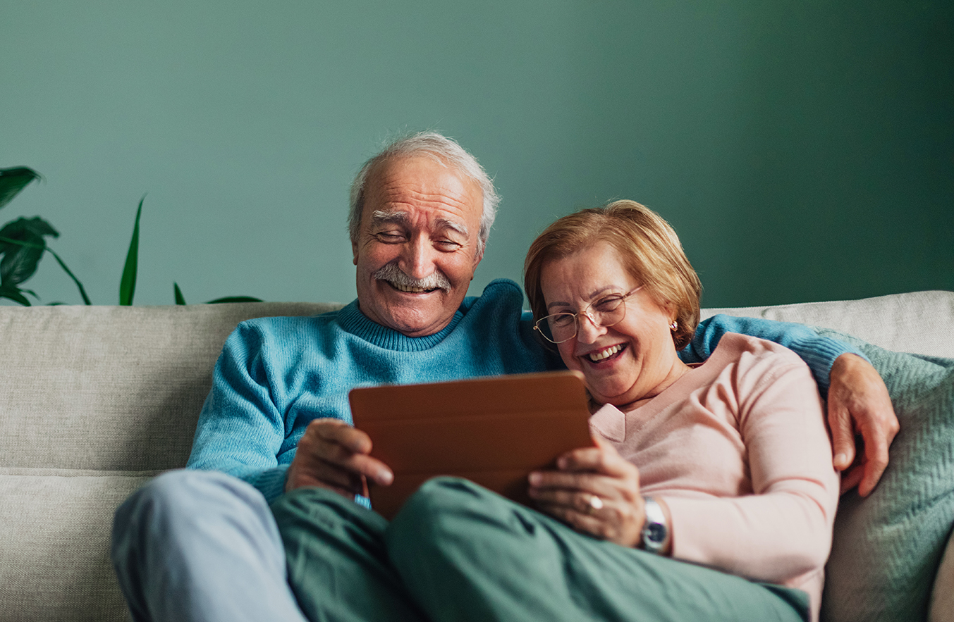 Older man and woman smiling while looking at an electronic tablet. Get Online Week logo in lower right corner.